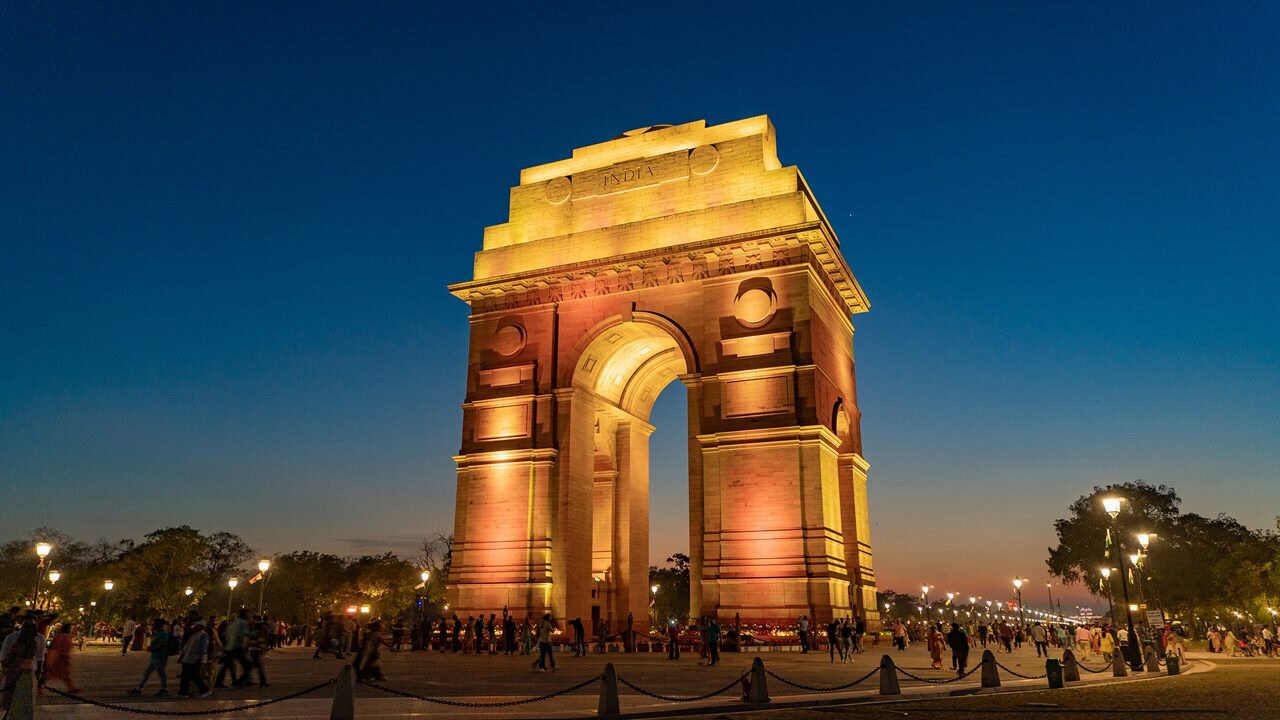 India Gate in New Delhi at dusk, with the canopy lit and people crossing the forecourt