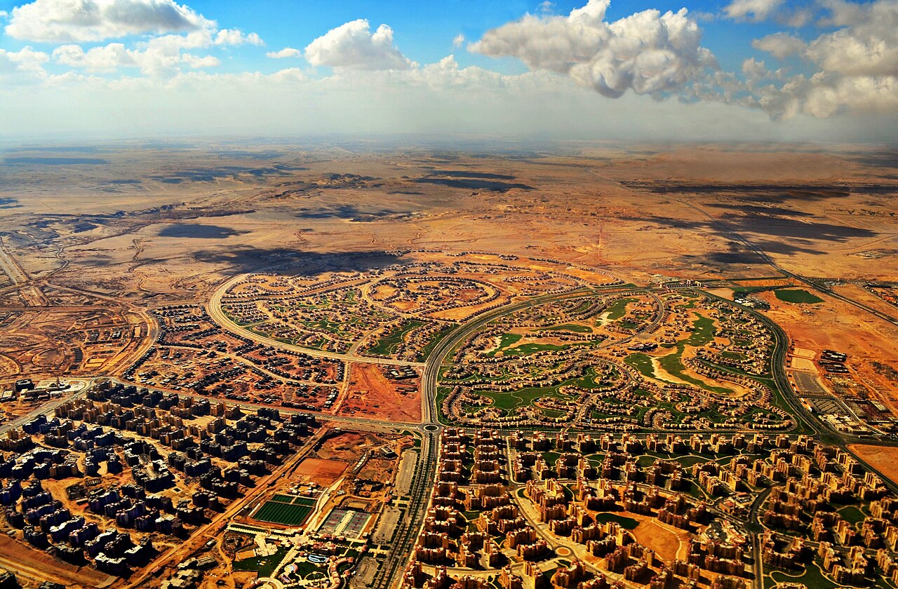 Low residential blocks and villas in a New Cairo compound, with open desert beyond the planted edge