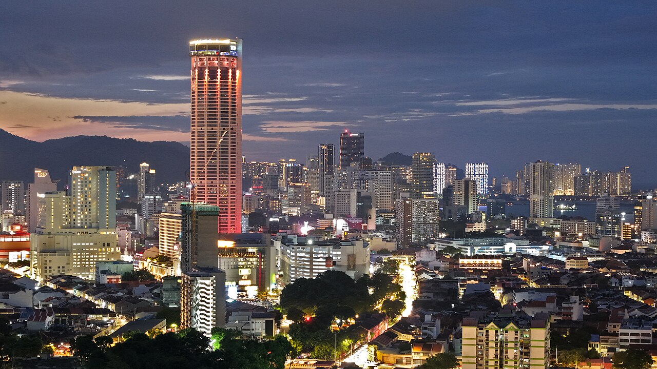 George Town at dusk, with a tall residential tower, low roofs and hills
